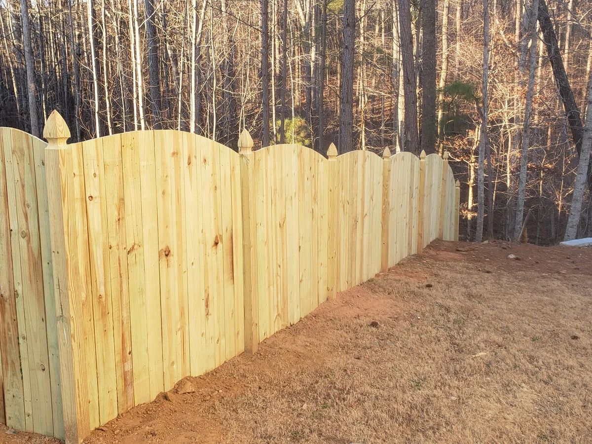 New scalloped wood privacy fence along a wooded backyard