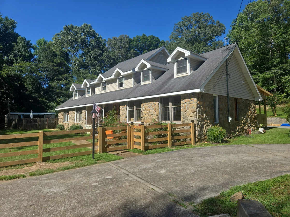 Stone house with a new dark shingle roof and dormers, seen from the driveway